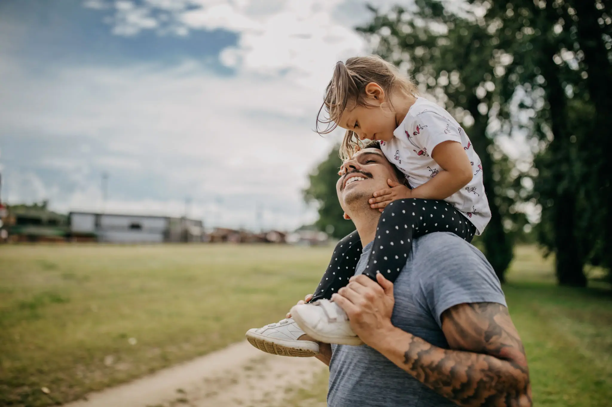 Father carries daughter on shoulders outdoors on a cloudy day.