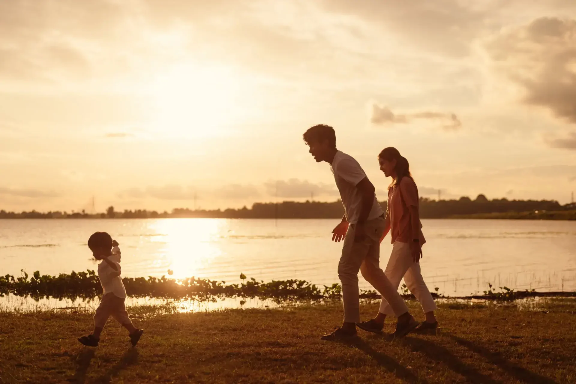 Family walking and playing near a lake during sunset.