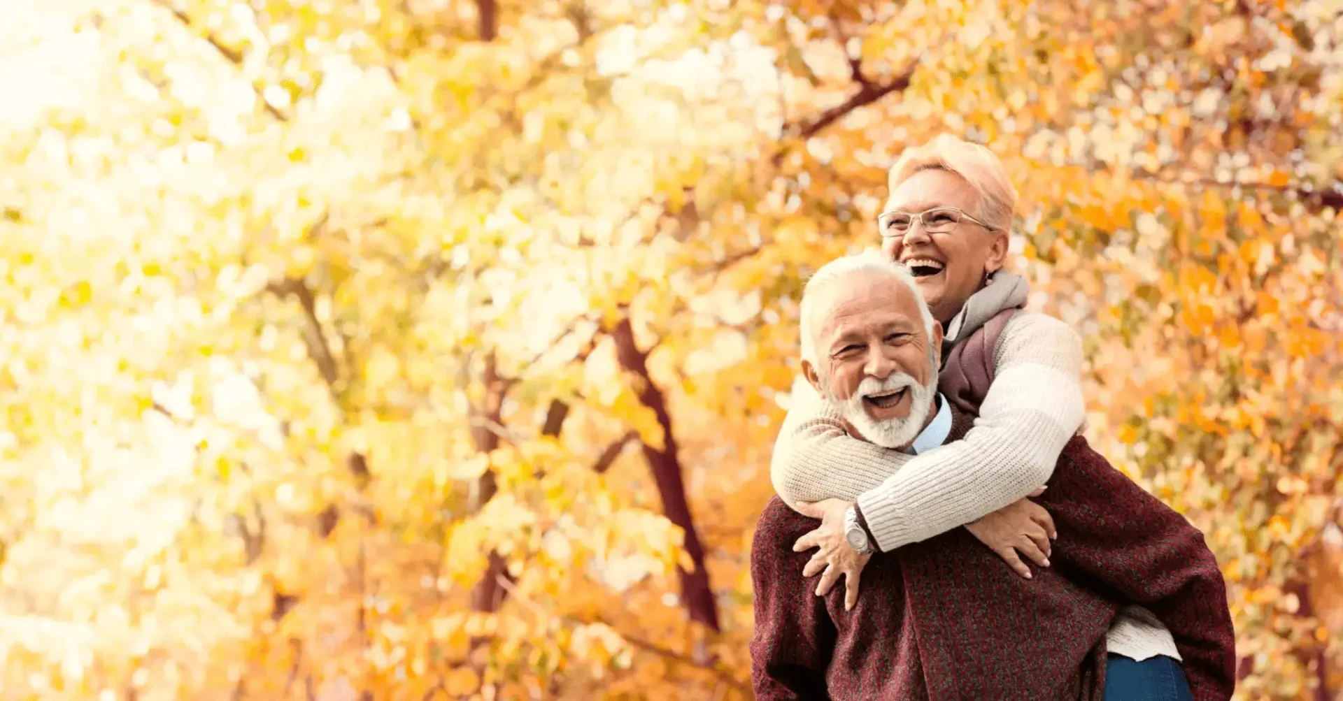 Happy elderly couple enjoying a piggyback ride in autumn.