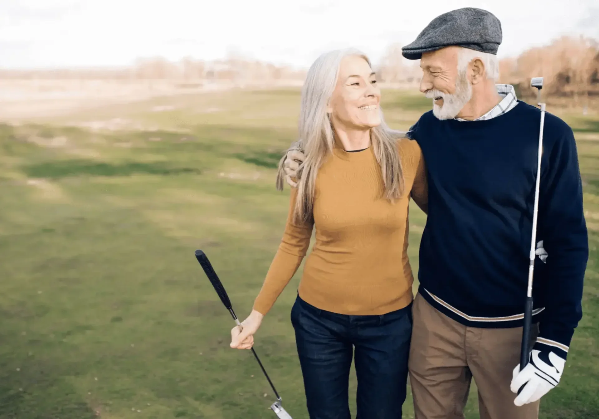 Elderly couple walking outdoors, smiling and holding golf clubs.